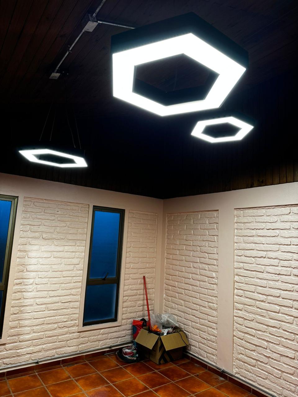 Sala con luminarias hexagonales suspendidas y muros de ladrillo pintado, Fundación Nuestros Hijos