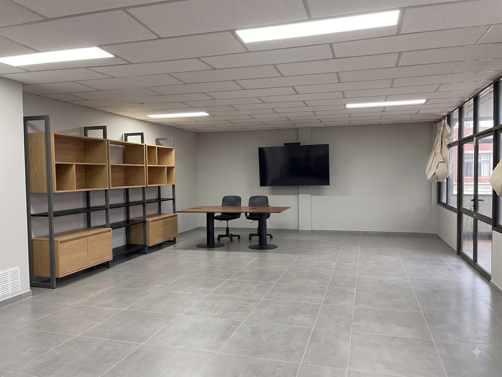 Espacio colaborativo con estanterías, mesa de reuniones y pantalla, remodelado en la UMCE